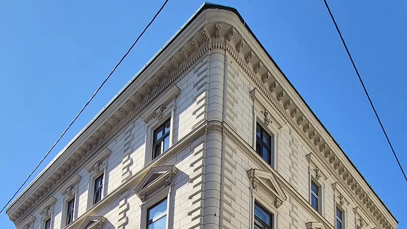 Eine historische Gebäudeecke in Beige mit kunstvollen Details vor einem strahlend blauen Himmel. Große Fenster und dekorative Verzierungen vermitteln Eleganz und Erhabenheit.